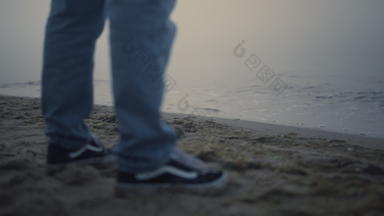 的家伙腿运动鞋站海海滩未知的男人。脚穿休闲鞋子